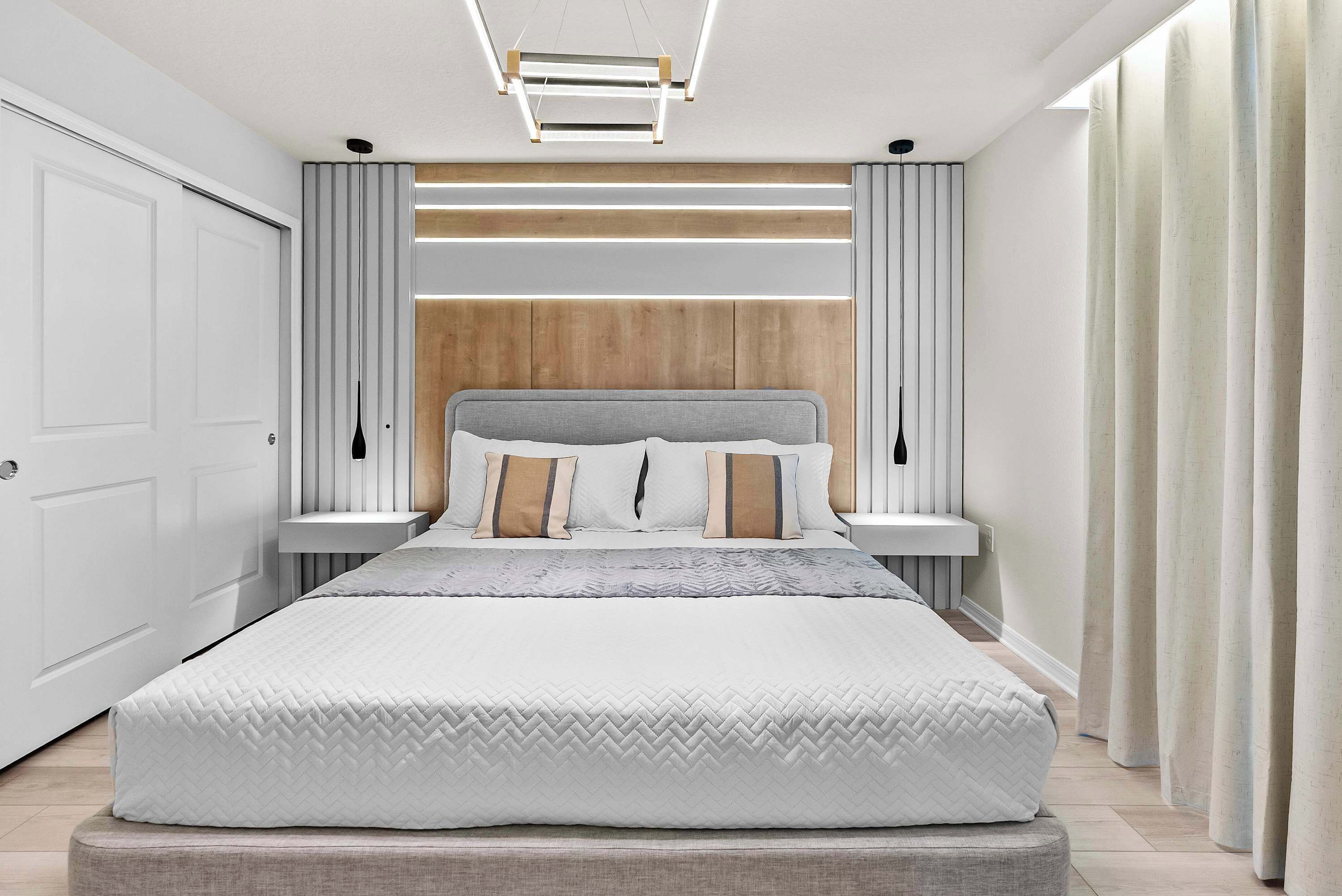 A modern bedroom with a large bed, bedside tables, and a headboard with built-in lighting.