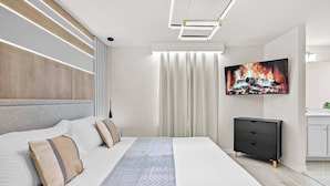 Ein modernes Schlafzimmer mit einem großen Bett, einem Flachbildfernseher und einer schlichten Kommode.