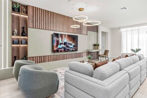 Ein modernes Wohnzimmer mit großem Flachbildfernseher, grauen Sofas und einer Wand als Holzdekor.