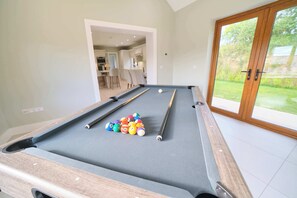 A pool table with balls and cues, a doorway leading to a dining area, and a sliding glass door to a garden. - Deluxe 4 Bedroom New Build with Games Room & Private Garden By Travel Lets Holiday Homes Letterkenny (Letterkenny)