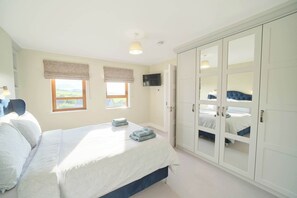 A bedroom with a bed, two windows with curtains, a wardrobe, and a television.
