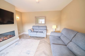 A living room with a flat-screen TV, a fireplace, a sofa, a mirror, and a lamp. - Deluxe 4 Bedroom New Build with Games Room & Private Garden By Travel Lets Holiday Homes Letterkenny (Letterkenny)