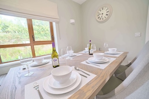 A dining table set with white plates, bowls, and cutlery, with a bottle of wine and glasses on it. - Deluxe 4 Bedroom New Build with Games Room & Private Garden By Travel Lets Holiday Homes Letterkenny (Letterkenny)