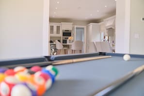 A pool table with balls, a kitchen area with cabinets, and a dining table with chairs.
