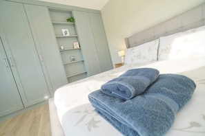 Ein Schlafzimmer mit Bett, Nachttisch, Lampe, Kleiderschrank und einem Regal mit Dekoration.