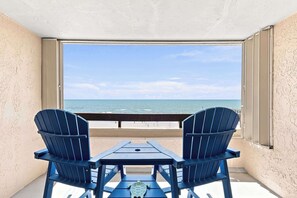 A balcony with two Adirondack chairs and a table, overlooking a beach with the ocean and a clear sky. - Serenity at Sea Pointe Oceanfront Condo with Pool (North Myrtle Beach)