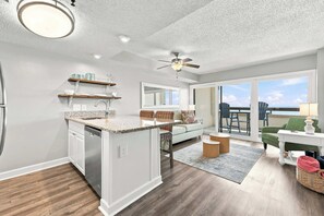 A modern kitchen with a built-in dishwasher, wooden shelves, and a dining area with a view. - Serenity at Sea Pointe Oceanfront Condo with Pool (North Myrtle Beach)