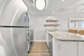 A modern kitchen with stainless steel appliances, wooden shelves, and a granite countertop.