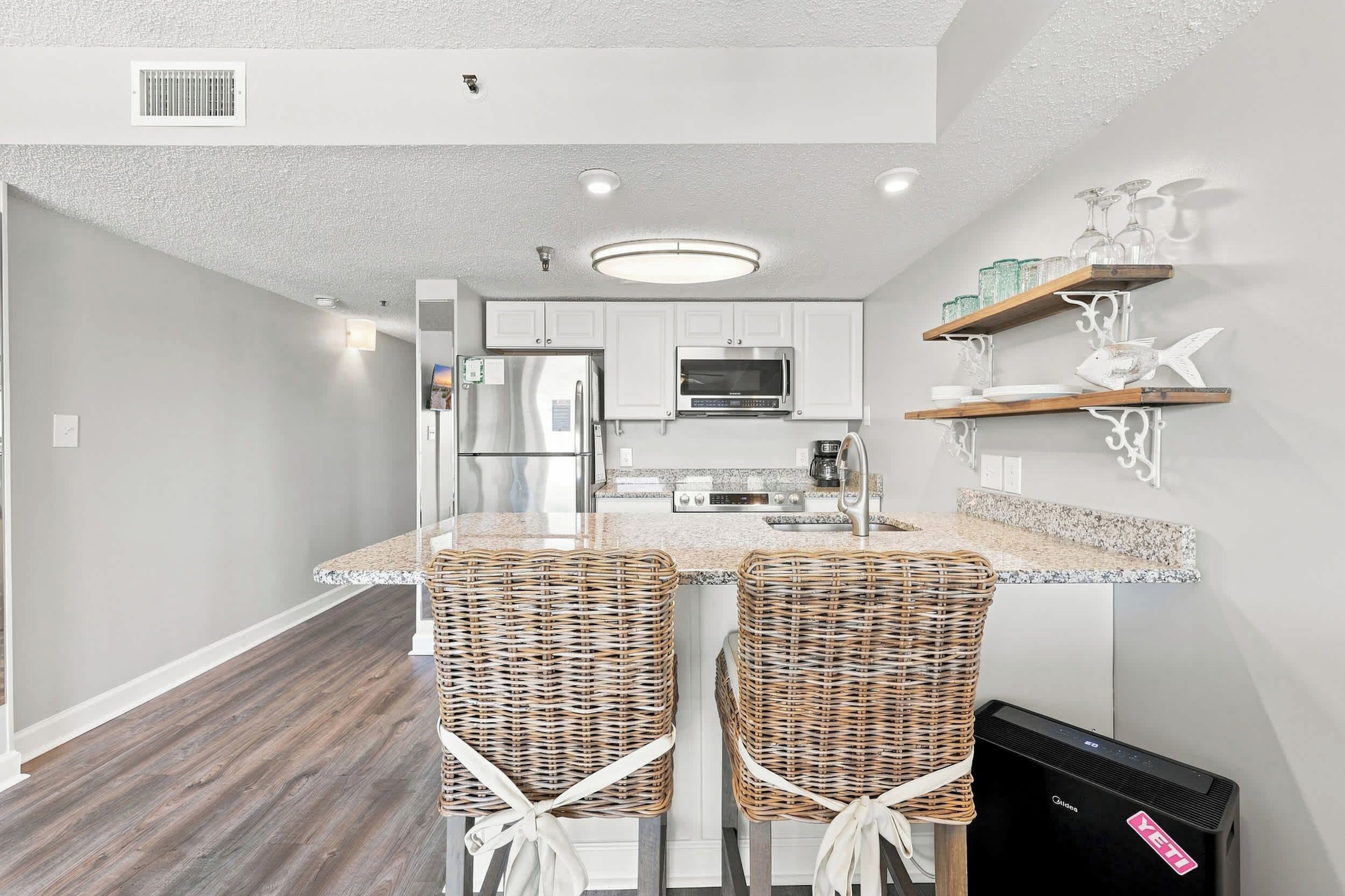 A modern kitchen with a central island, stainless steel appliances, and a dining area with wicker chairs.