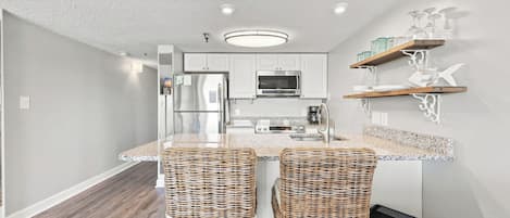 A modern kitchen with a central island, stainless steel appliances, and a dining area with wicker chairs.