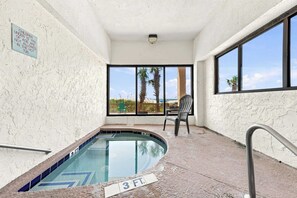 An indoor swimming pool with a 3 FT depth marker, a chair, and a view of palm trees through large windows. - Serenity at Sea Pointe Oceanfront Condo with Pool (North Myrtle Beach)