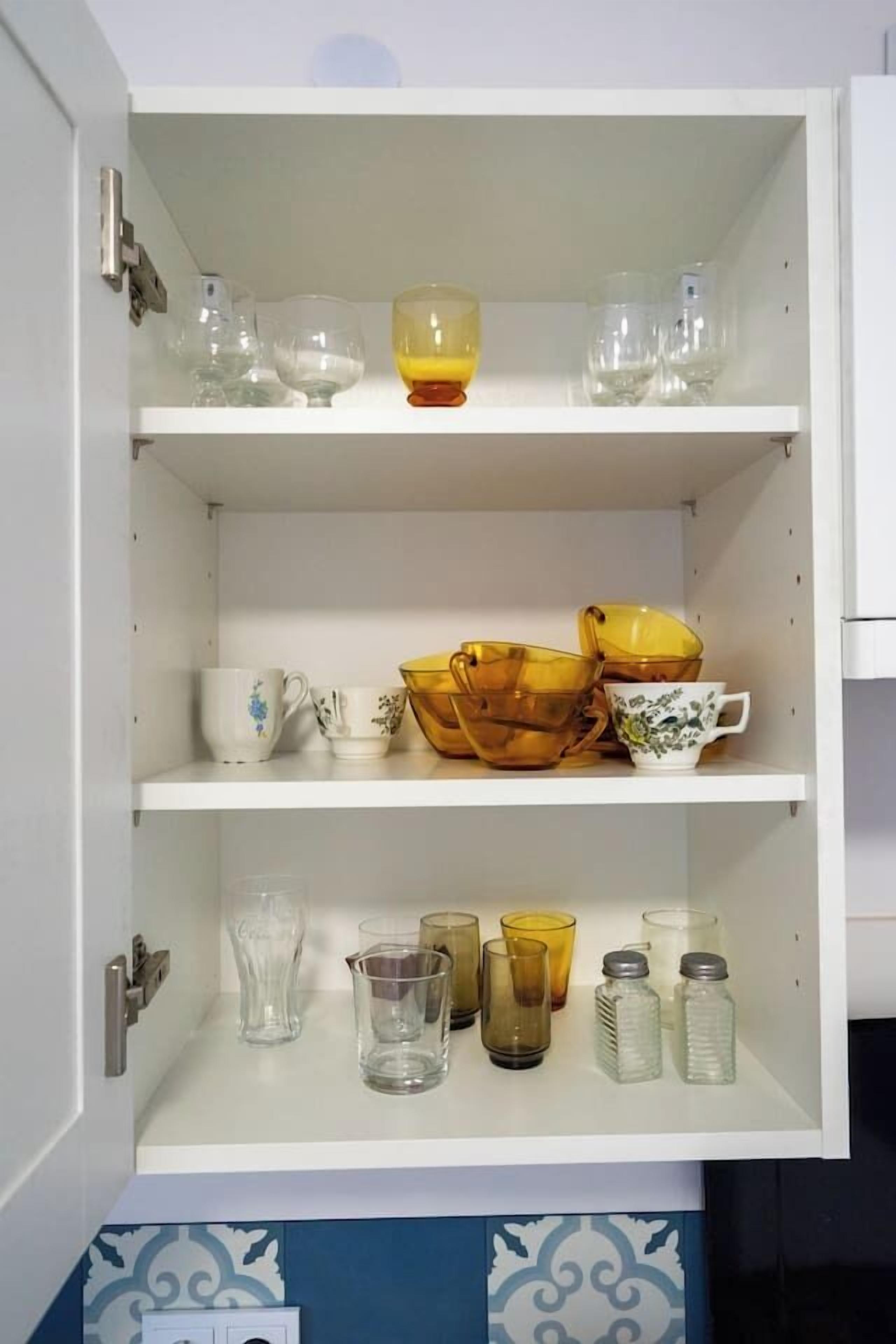 A white cabinet with multiple shelves containing various glassware and ceramic items.