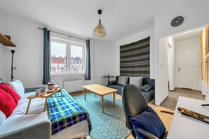 A modern living room with a sofa, a coffee table, and a chair. There is a window with curtains, a radiator, and a wall-mounted lamp. - Warsaw Downtown Studio- Top location, Metro Nearby (Warsaw)