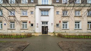 Ein Gebäude mit einem zentralen Eingang, mehreren Fenstern und einem gepflasterten Weg, der zur Tür führt.