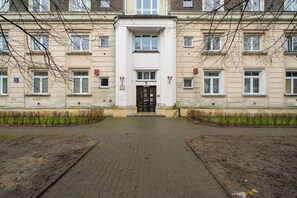 Ein Gebäude mit einem zentralen Eingang, mehreren Fenstern und einem gepflasterten Weg, der zur Tür führt.