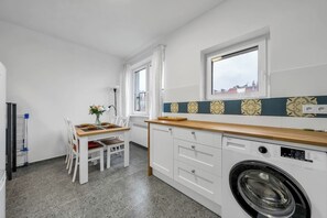 A compact kitchen with a washing machine, a dining table with chairs, and a window with curtains. - Warsaw Downtown Studio- Top location, Metro Nearby (Warsaw)