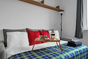 A neatly made bed with a plaid bedspread, a bedside table with a coffee pot and cups, and a lamp on the nightstand. - Warsaw Downtown Studio- Top location, Metro Nearby (Warsaw)