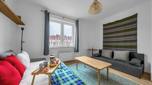 Ein modernes Wohnzimmer mit einer Couch, einem Holztisch, einer Bank und Blick auf Gebäude durch ein Fenster.