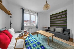 Ein modernes Wohnzimmer mit einer Couch, einem Holztisch, einer Bank und Blick auf Gebäude durch ein Fenster.