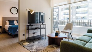 A modern hotel room with a bed, a TV on a stand, a round coffee table, a green sofa, and a balcony with a view of the city. - Inés Matte Urrejola Apartments by Andes STR (Providencia)