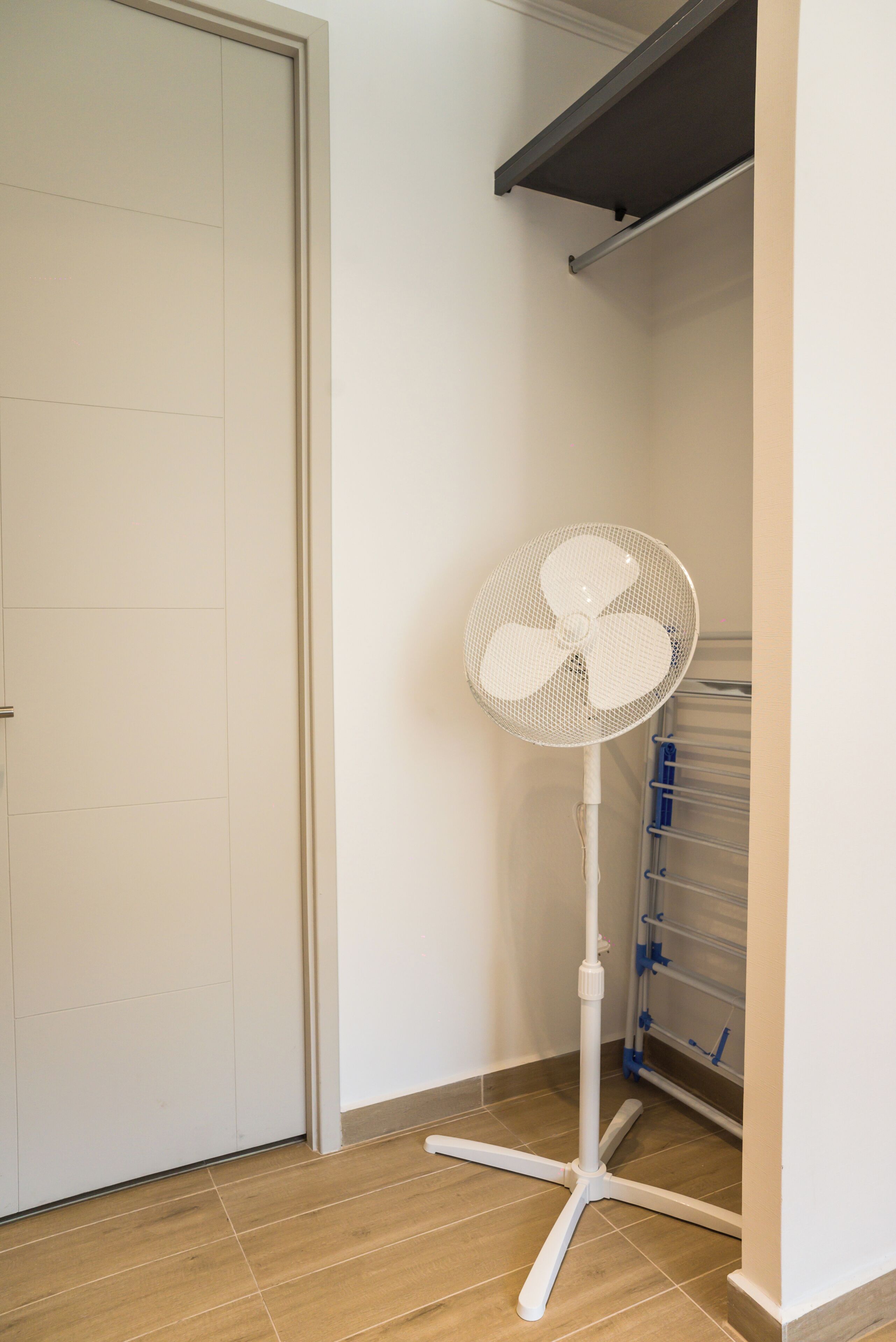 A room with a white door, a standing fan, and a shelving unit against the wall.