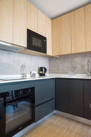 A modern kitchen with wooden cabinets, a black microwave, a coffee maker, and a dishwasher. - Inés Matte Urrejola Apartments by Andes STR (Providencia)