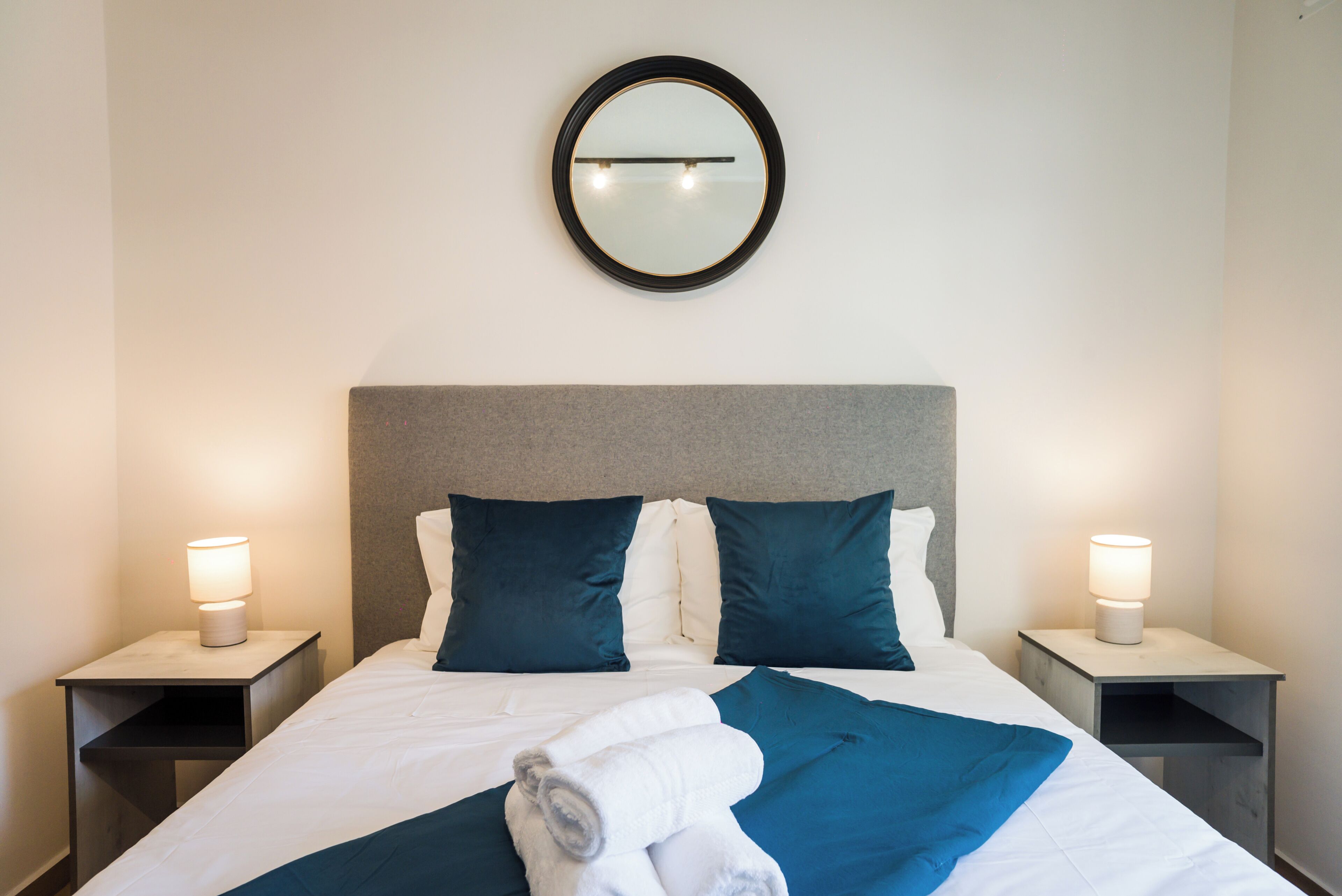 Una habitación de hotel con cama, dos mesitas de noche, un espejo y dos lámparas.
