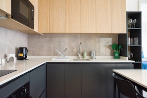 A modern kitchen with a microwave, kettle, and a sink with a faucet. - Inés Matte Urrejola Apartments by Andes STR (Providencia)