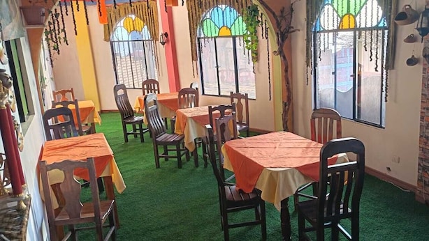 A dining area with tables and chairs, green artificial turf flooring, and large windows with decorative elements.