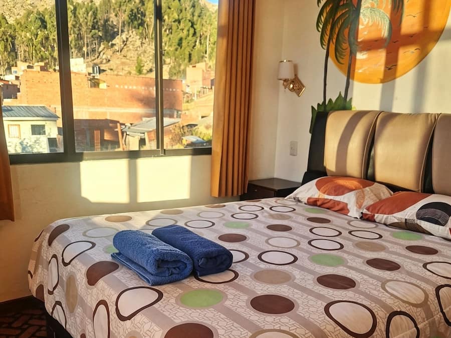 Ein Hotelzimmer mit Bett, Fenster mit Blick auf eine gebirgige Landschaft und einer Wand mit Palmenmotiv.