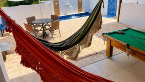 Un área junto a la piscina con hamaca, mesa de billar y mobiliario exterior.