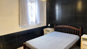 Un dormitorio con cama, mesita de noche, ventana con cortinas y pared con diseño texturizado negro.