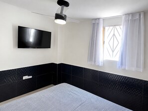 Un baño moderno con pared de azulejos blancos y negros, un televisor montado y una ventana con cortinas traslúcidas.