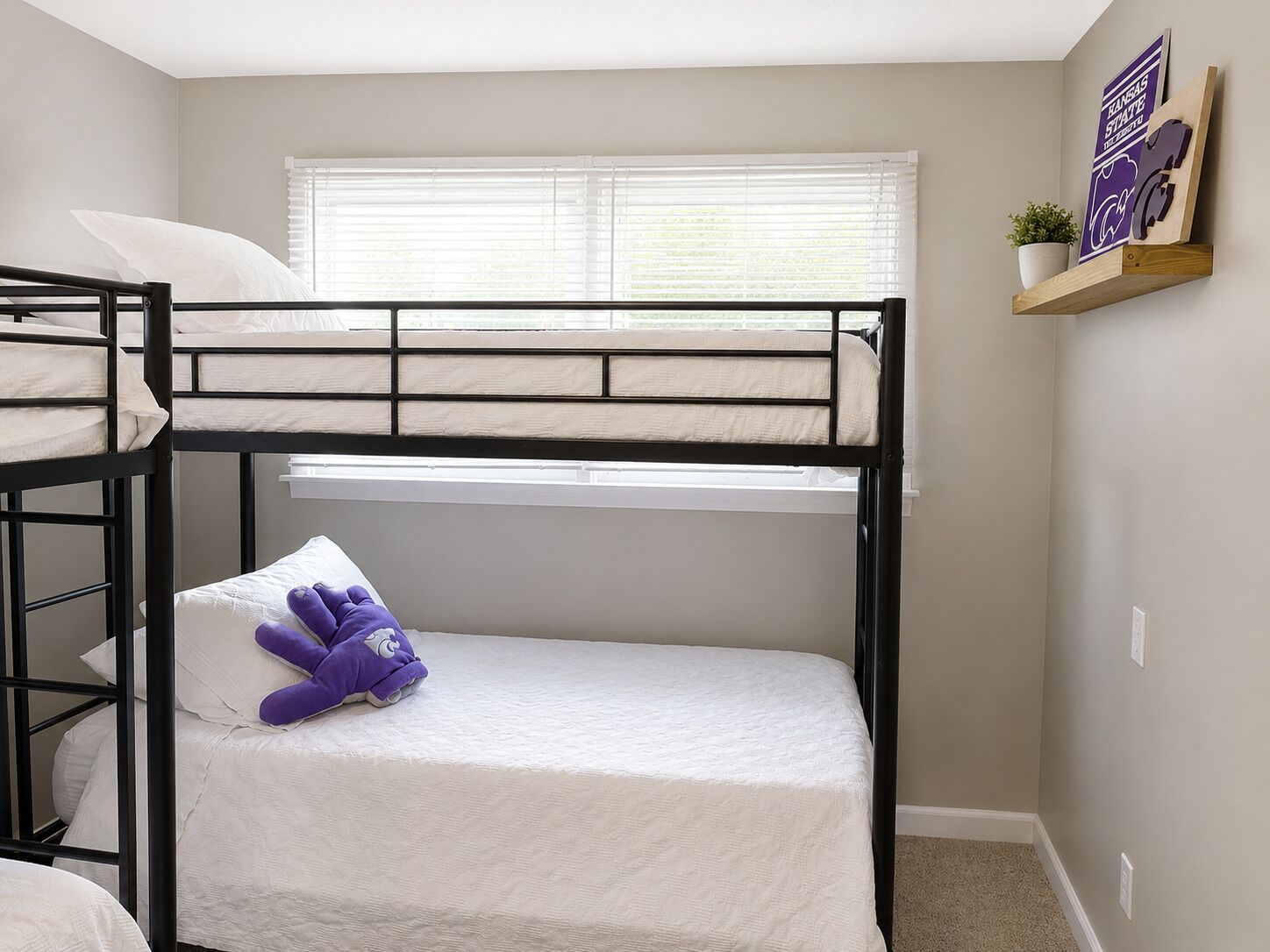 A bunk bed room with a window, a shelf with a plant, and a poster on the wall.