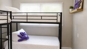 A bunk bed room with a window, a shelf with a plant, and a poster on the wall.