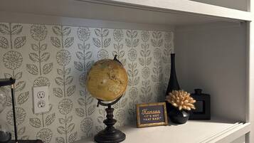 Una estantería con un globo terráqueo, un cartel enmarco y un florero con flores secas, todo sobre un papel tapiz con estampado de hojas.