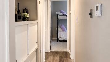 A narrow hallway with wooden flooring, a bunk bed in the background, and a white door on the left.