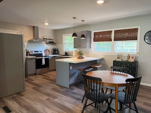 A modern kitchen with a central island, dining area with chairs, and a clock on the wall.