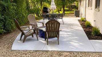 An outdoor patio with Adirondack chairs, a table, and a grill.