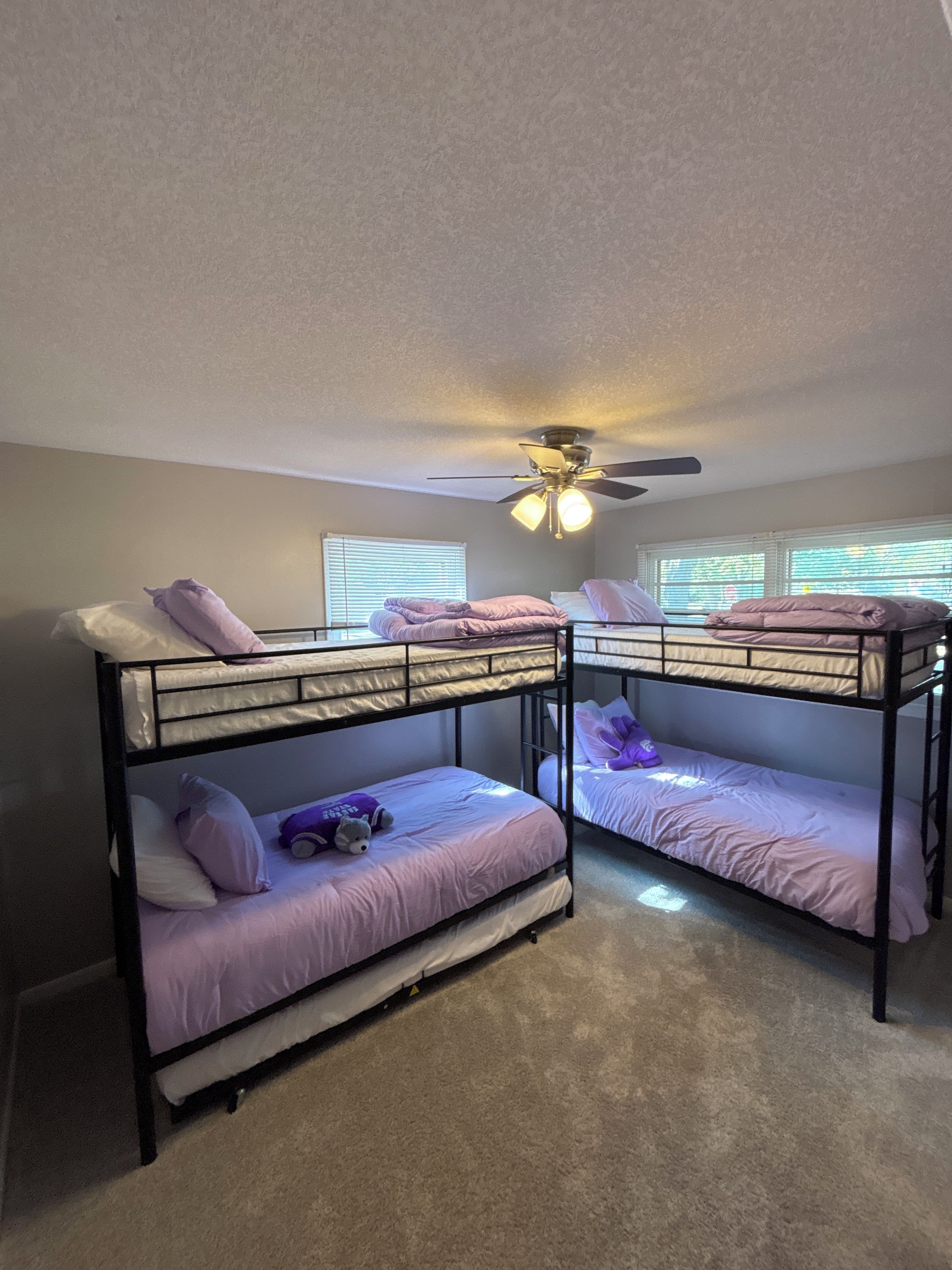 A room with bunk beds, a ceiling fan, and windows with blinds.