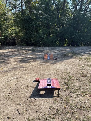 Two wooden bean bags in a dry, grassy field with trees in the background.