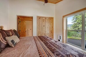 Ein Schlafzimmer mit einem großen Bett, einem Holzschrank und einem Fenster mit Blick auf Grünflächen.