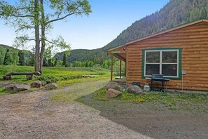 A wooden cabin with a porch, surrounded by a natural landscape with trees and a mountain in the background. - Ponderosa | Creekside Cabin Near Wolf Creek (South Fork)