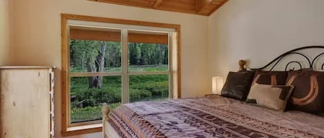 Une chambre avec une grande fenêtre, un lit avec une literie à motifs et un plafond en bois.