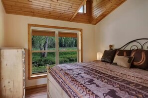 Ein Schlafzimmer mit großem Fenster, einem Bett mit gemusterten Betttextilien und einer Holzbalkendecke.