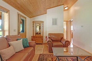 A living room with a wooden ceiling, a brown leather sofa, a glass coffee table, and a patterned rug. - Ponderosa | Creekside Cabin Near Wolf Creek (South Fork)