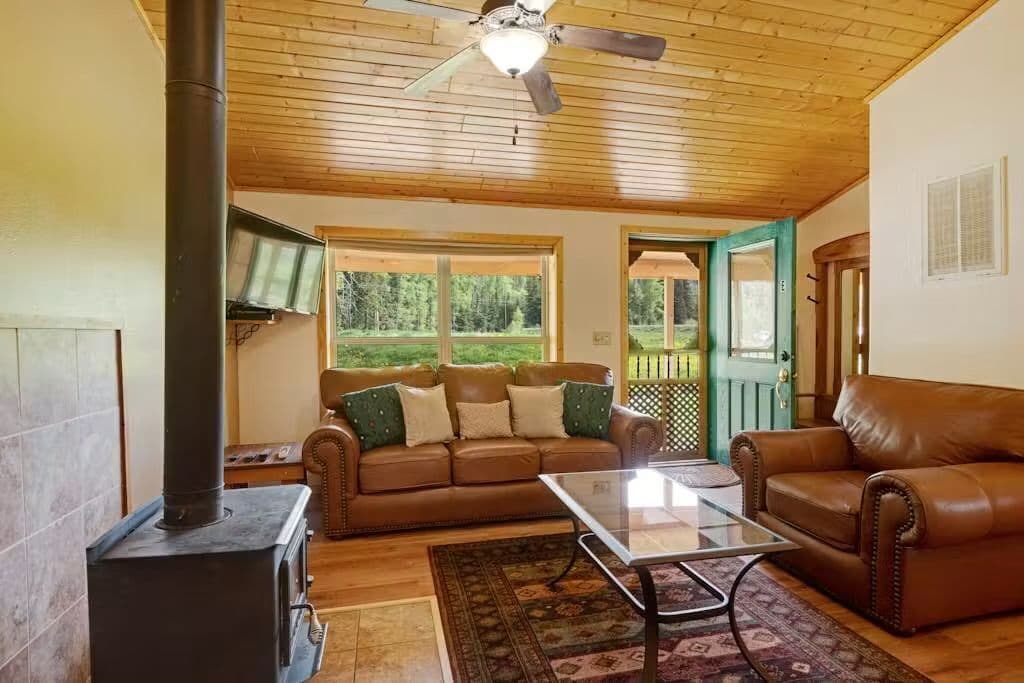A cozy living room with a fireplace, leather sofas, a glass coffee table, and a wooden ceiling.