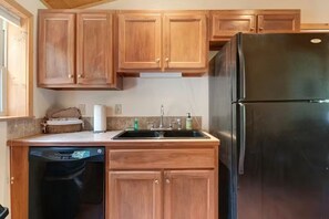 Eine Küche mit Holzausstattung, einem schwarzen Kühlschrank, einem Geschirrspüler und einem Waschbecken mit Armatur.
