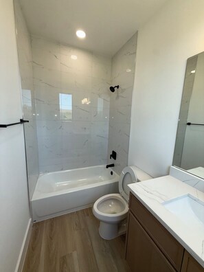 A modern bathroom with a bathtub, toilet, and a vanity with a mirror. - Arlington Park Estate - 3BR Luxury [Coming Soon!] (Dallas)