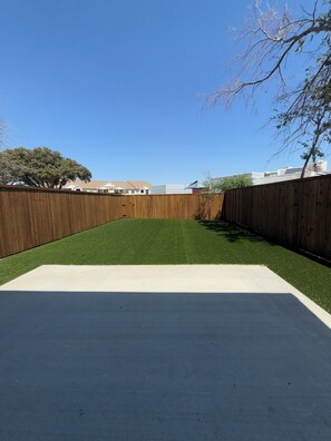 A backyard with artificial grass, a wooden fence, and a tree. - Arlington Park Estate - 3BR Luxury [Coming Soon!] (Dallas)